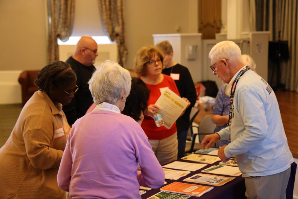 Older adults stand around a table with flyers for all of Erie County RSVP's partner organizations
