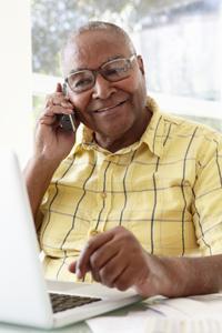 man at computer speaking on cell phone