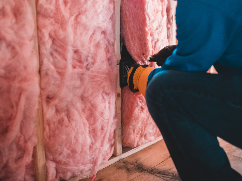 Pink insulation being installed into a wall cavity by a worker.